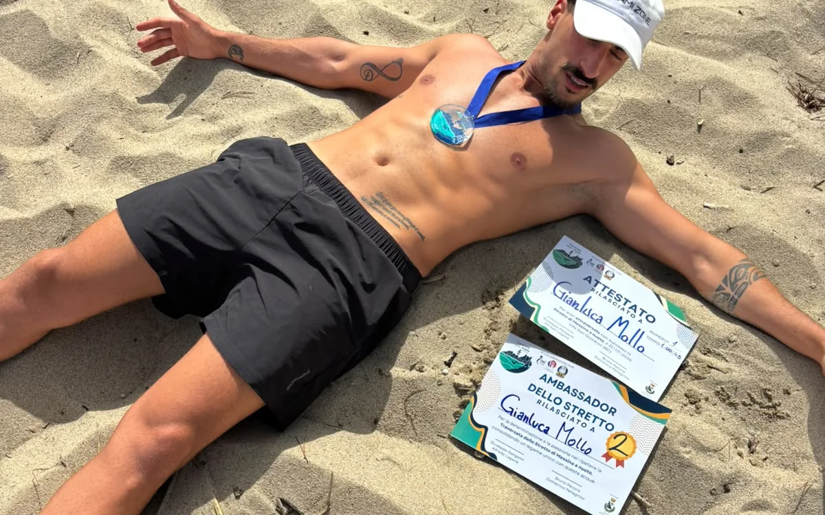 Gianluca Mollo sulla sabbia con medaglia e attestati dopo la traversata dello Stretto di Messina